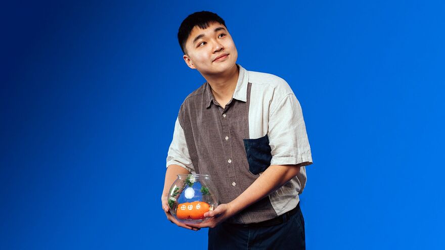 Jin Hao Li standing over a blue background holding a fishbowl