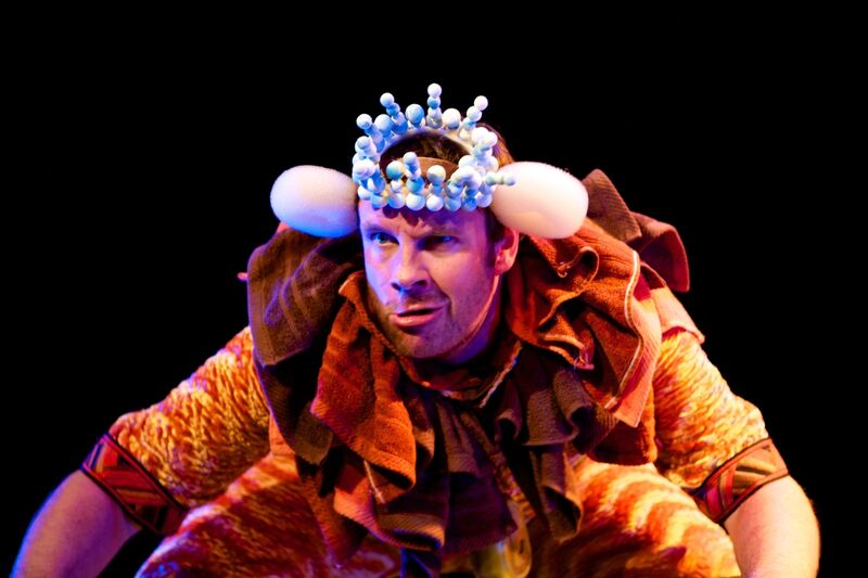 A man dressed as a lion crouches with a grimace on his face