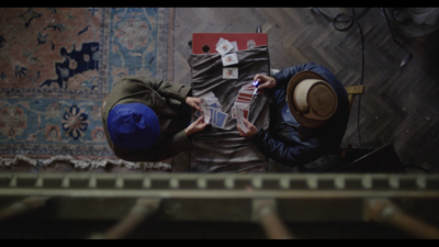 Two people are playing a game of cards. We are looking directly at them from above so can see the cards in their hands and on the table as well as the top of their heads