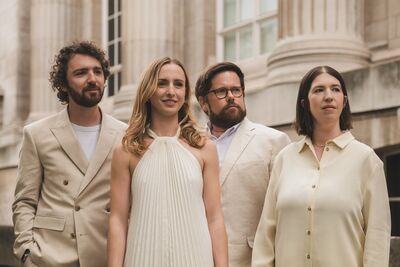 Castalian Quartet dressed in smart white outfits standing in front of a grand building