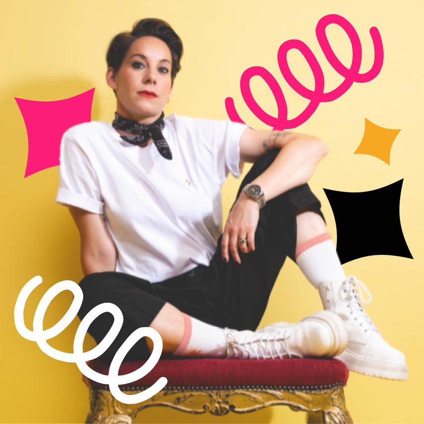 Suzi Ruffell sitting on a red chair with her knees up. Wearing a white t-shirt and with pink and white spirals around her