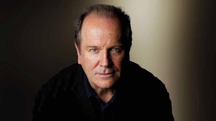 William Boyd looking forward wearing a black shirt, with a moody black and grey background