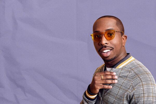 Kiell in tinted sunglasses and a smart jacket against a purple background