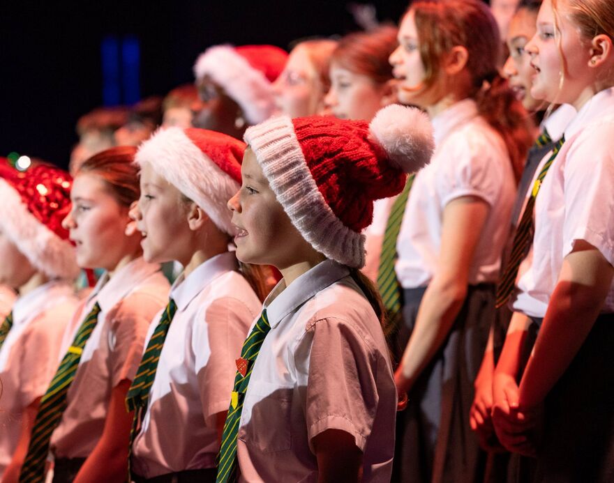 Children singing on stage wearing santa hats