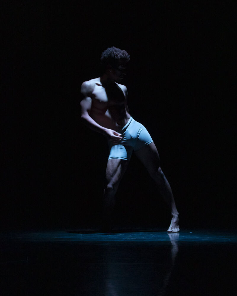 Liam Francis wearing grey shorts lit from above by a spotlight