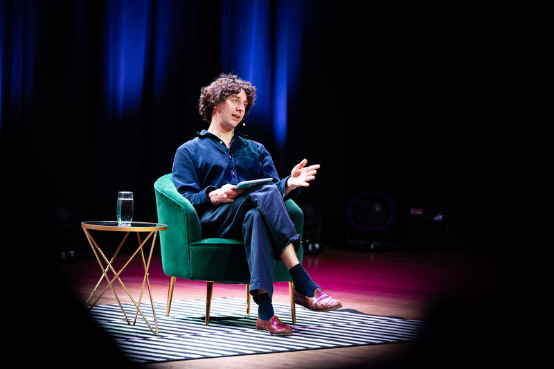 Merlin Sheldrake sitting in a green velvet chair on stage