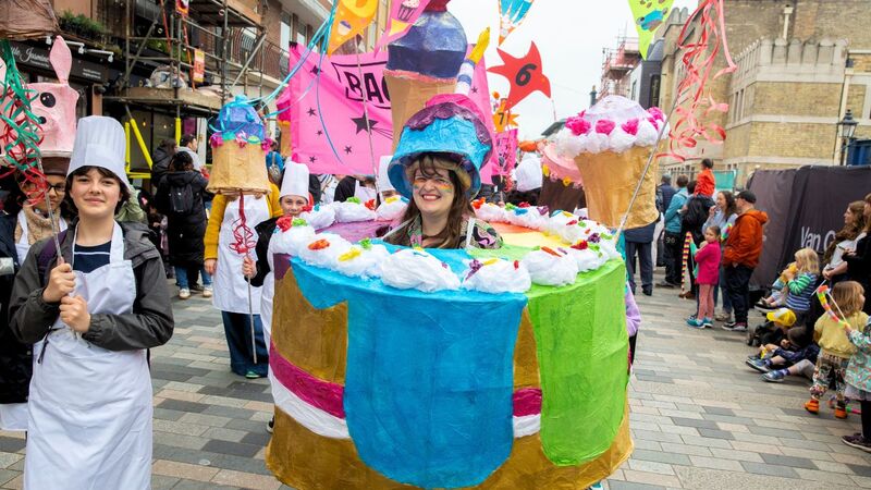A white woman stands in the middle of a giant papier mache cup cake