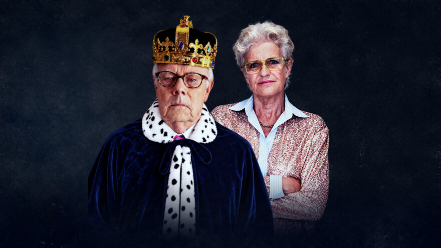 A man wearing a regal gown and crown, next to a woman wearing a pink shirt with her arms crossed 