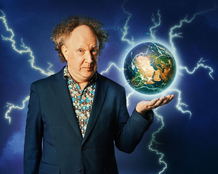 Andy Zaltzman wearing a blue patterned suit holding his hand up, with earth hovering above it and lots of lightening