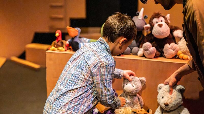 A little boy places a soft toy down on a cardboard box where other toys sit