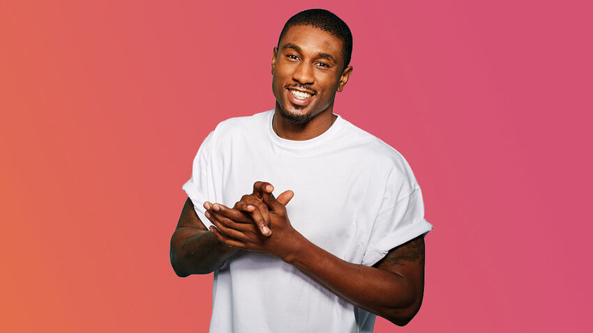 Ovie Soko standing and smiling, with a backdrop that blends from orange on the left to pink on the right