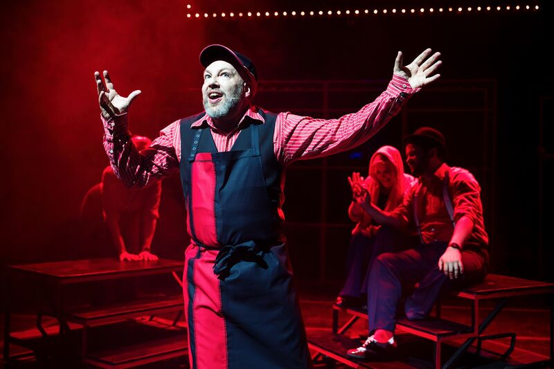 A man wearing a black and red apron stands with his arms outstretched