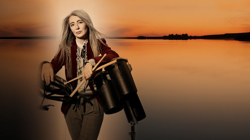 Evelyn Glennie holding drumsticks and percussion instruments overlayed on an image of a wide, calm lake