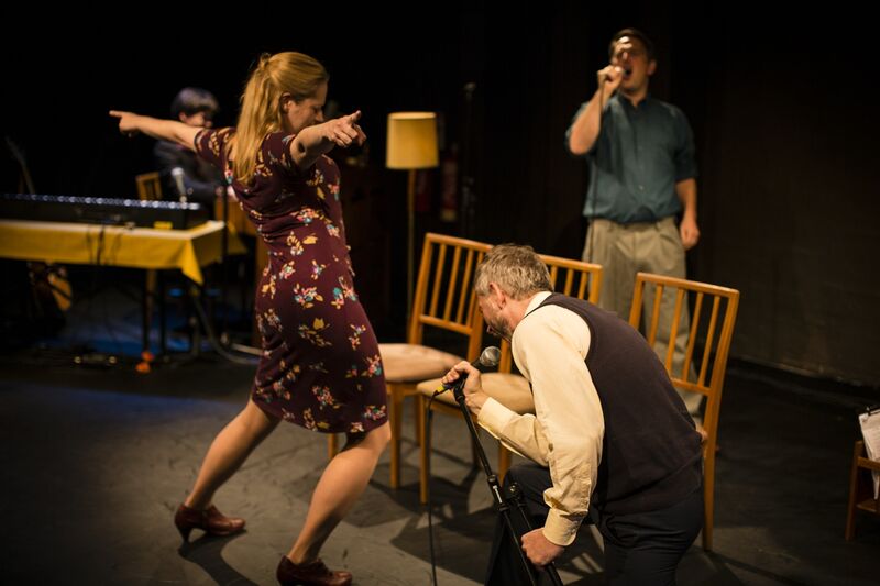 2 men and 1 woman pretend to perform a concert around a line of 3 chairs