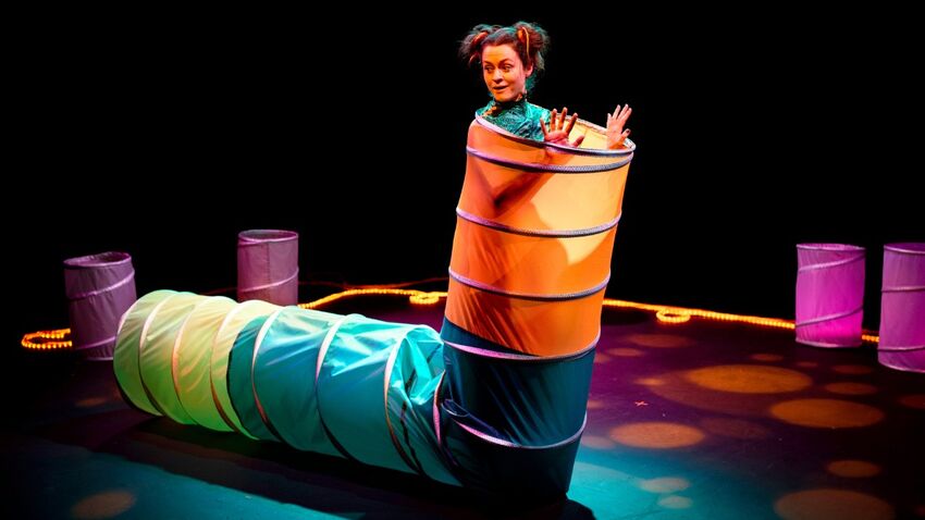 A performer emerges from a brightly coloured tube