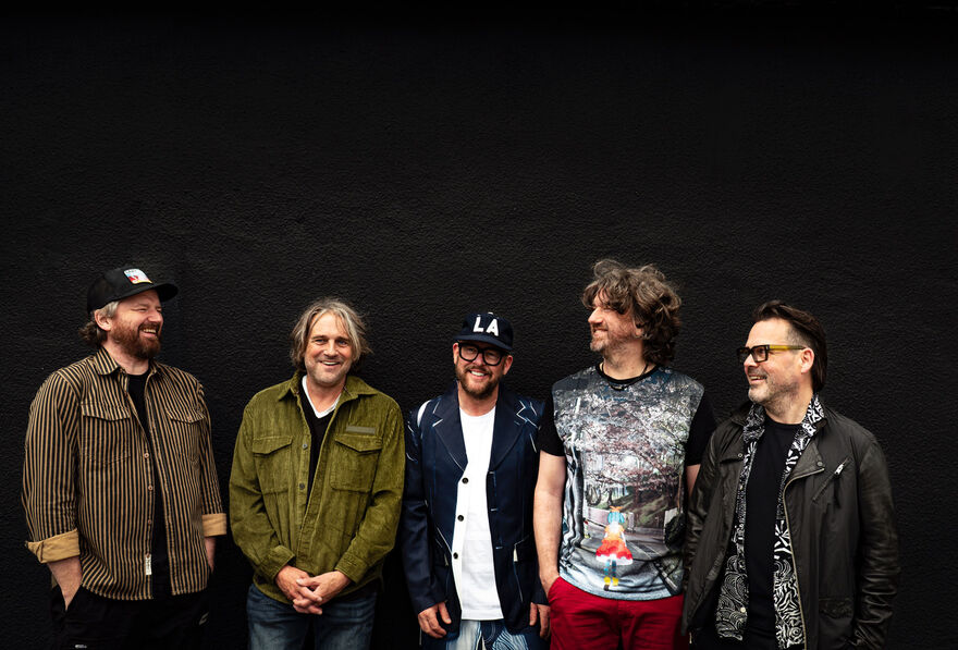 Group of 5 men standing over a black background. They are all smiling.