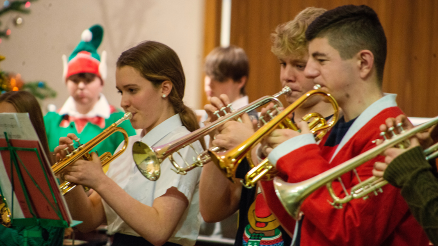 A group of young people play brass instruments. One of the students is dressed as an Elf