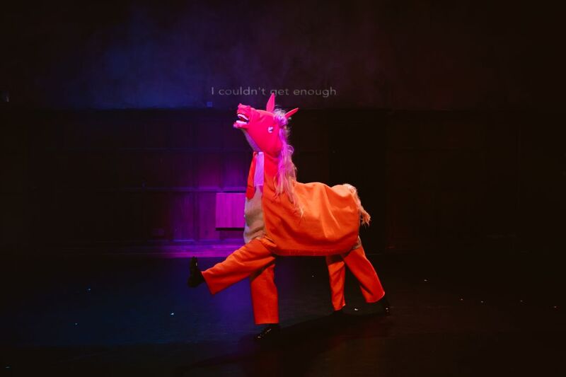 An orange pantomime horse on stage with one left up