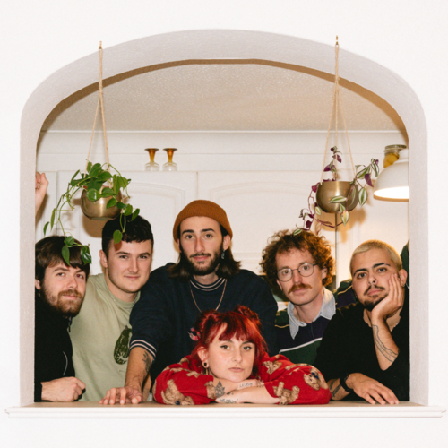6 people leaning through an arched window in a white wall