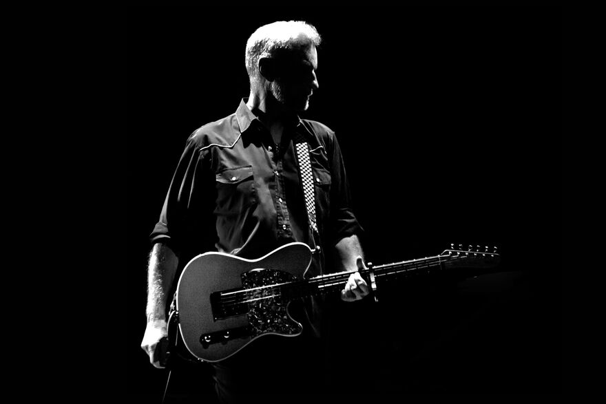 man in a black and white picture looks to the side while holding a guitar