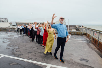 A group of older people stand in a line in a carpark, their arms are raised