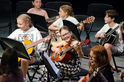 A group of children with guitars sitting and playing and smiling