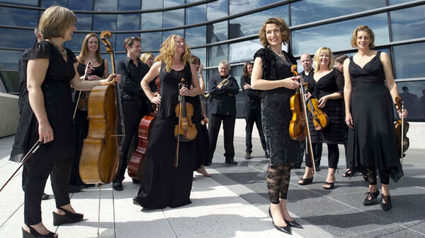 Musicians from Britten Sinfonia dressed in black stand outside a building carrying their instruments
