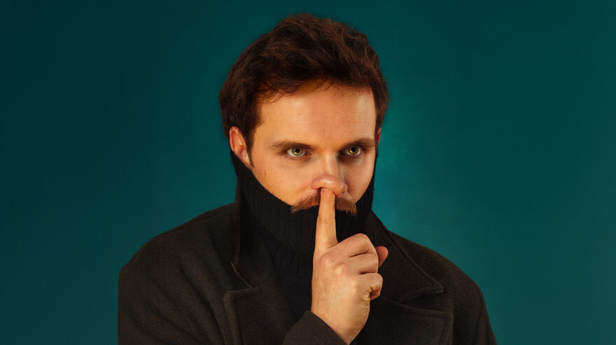 Vittorio Angelone over a blue background in a black coat, holding his finger up to his face