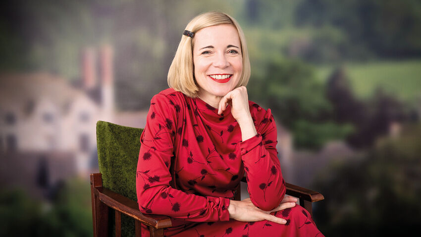 woman in red clothing smiles using her hand as a chin rest