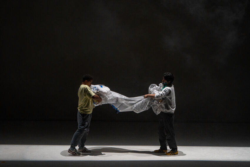 Two people facing each other both holding the same sheet of plastic