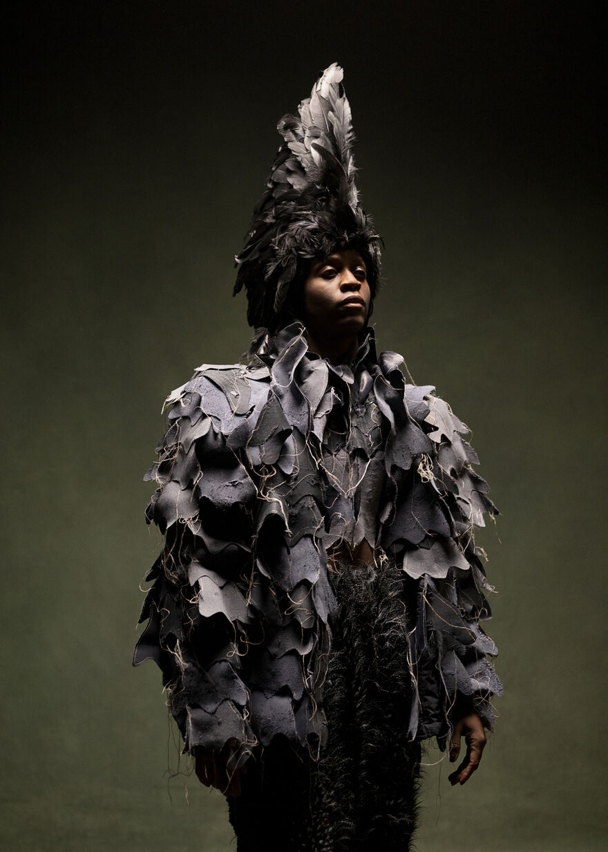 A black man wearing a feather headdress and a black feathery outfit