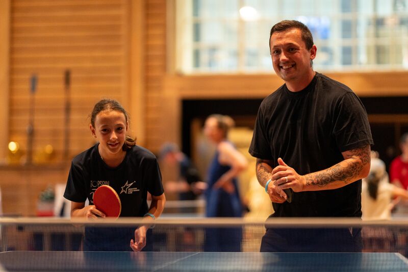 A girl and a man playing table tennis together on the same team. They are both smiling