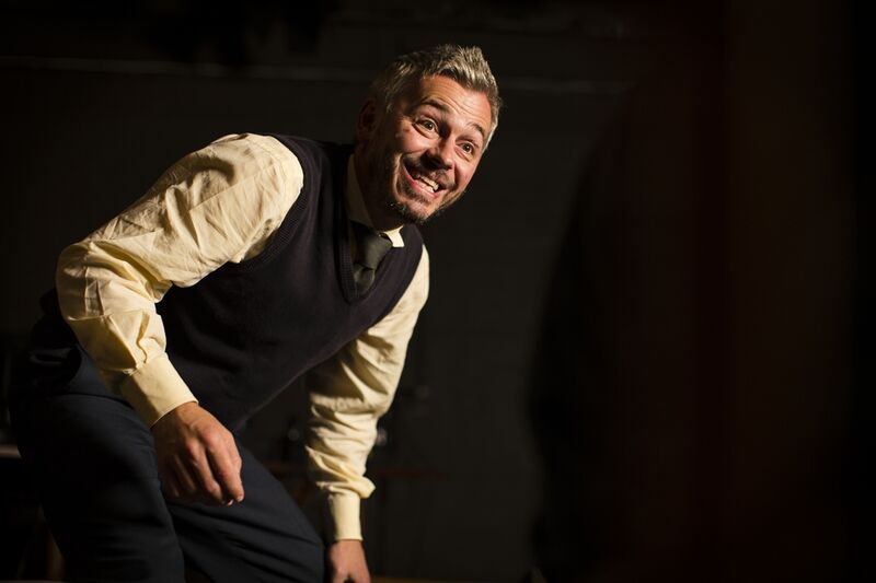 a man hunched over smiling manically to the side of the camera