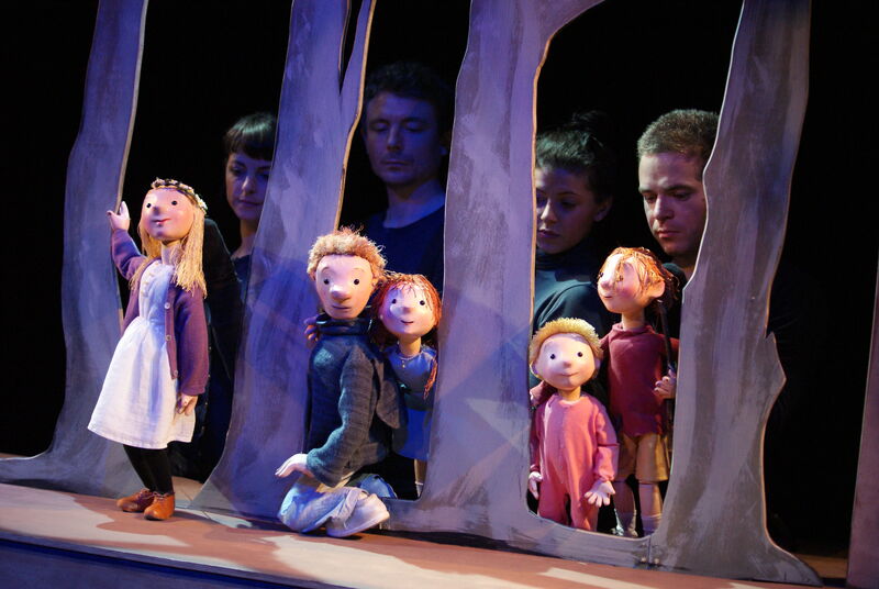 Wooden puppets of children and a father stand in between a cardboard set of trees