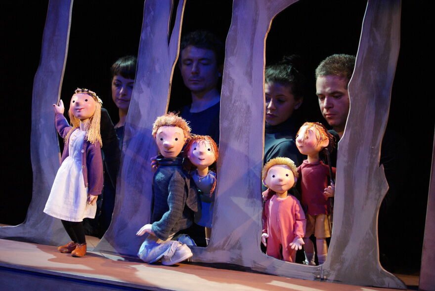 Wooden puppets of children and a father stand in between a cardboard set of trees