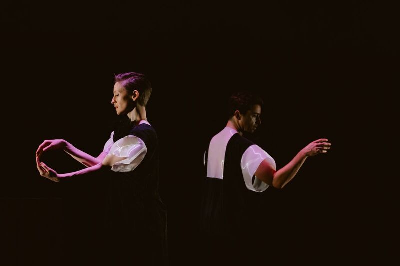 A profile picture of two dancers back to back with their arms in front of them
