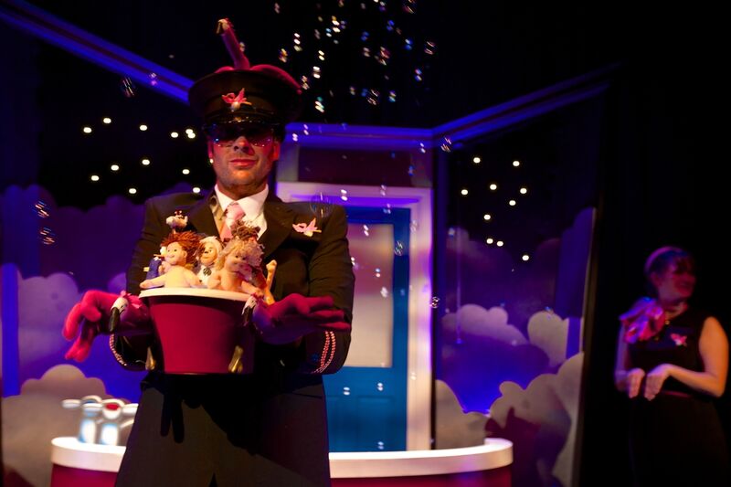 A man dressed in a conductor's uniform holds a bath with toy dolls inside