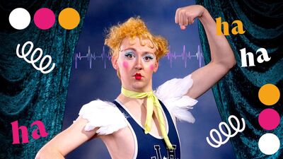 A person holding one arm up, with the other on their hip, wearing a blue vest and feather shoulder pads. They are wearing vibrant pink blush, red lipstick and blue eyeshadow