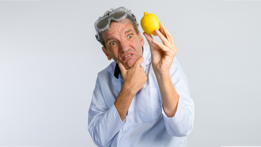Image of Henning Wehn holding a lemon, wearing science protective gear with a confused look on his face