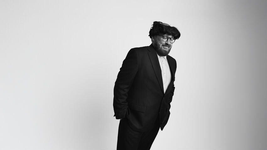 John Kearns wearing a black suit leaning to one side