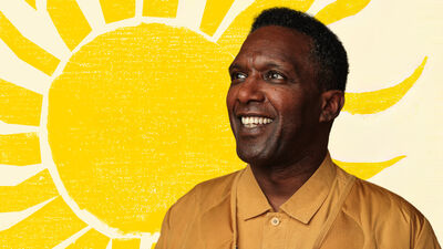 Lemn Sissay smiling in front of an illustration of a bright yellow sun