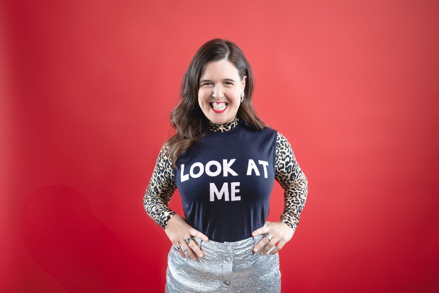 White lady smiling with her hands on her hips, with a t-shirt that has 'Look at me' on the front
