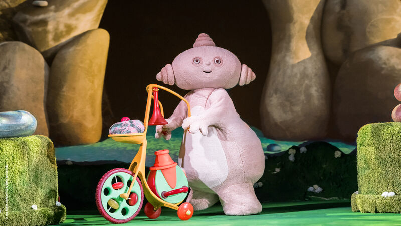 A small beige costumed creature pushes a multi-coloured tricycle