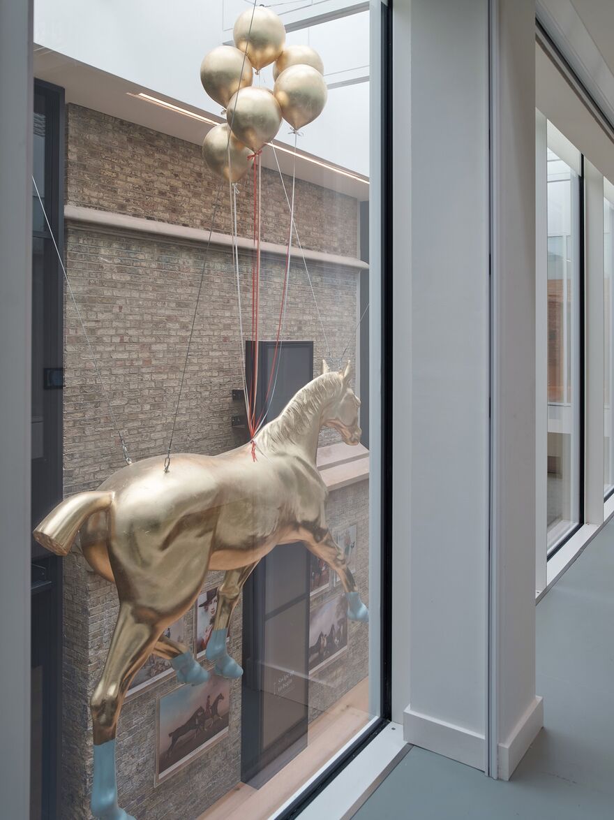 View through a big window of a golden horse statue held up by golden balloons