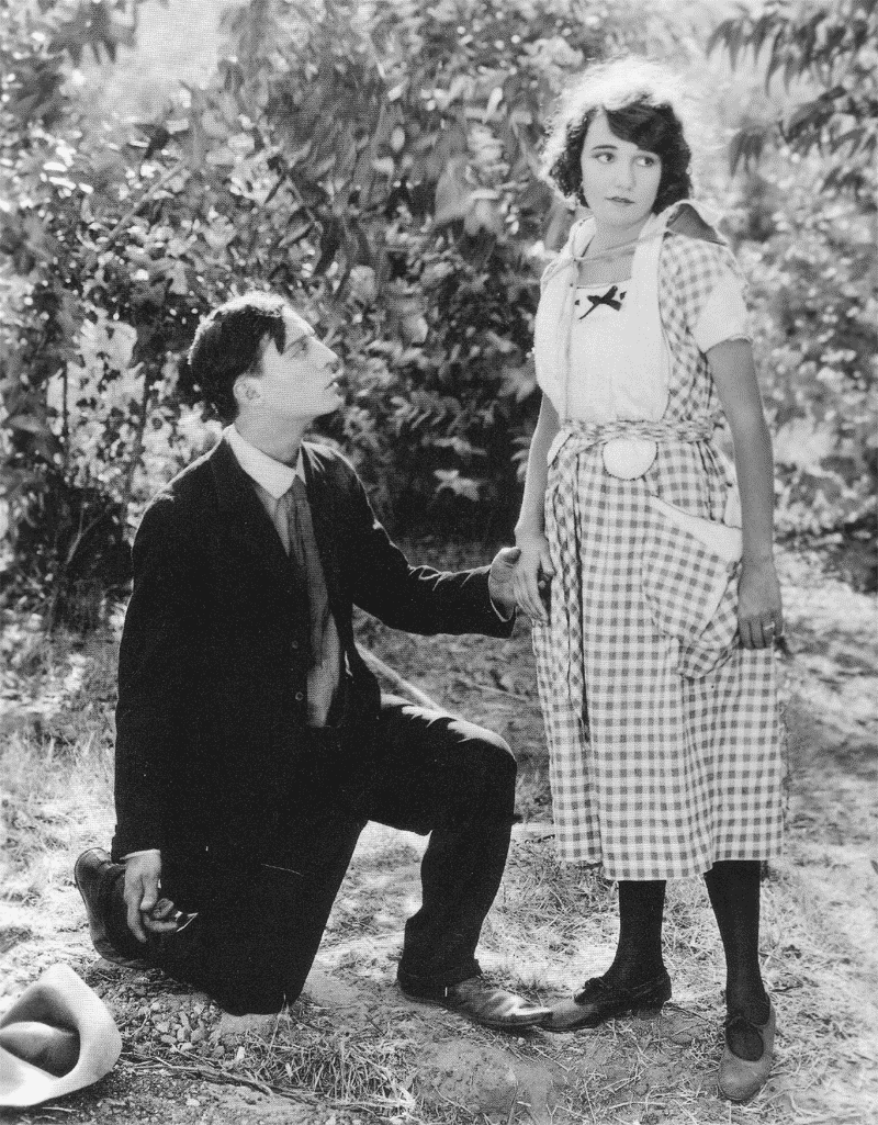 Old photo of a man on one knee looking at a women who looks concerned
