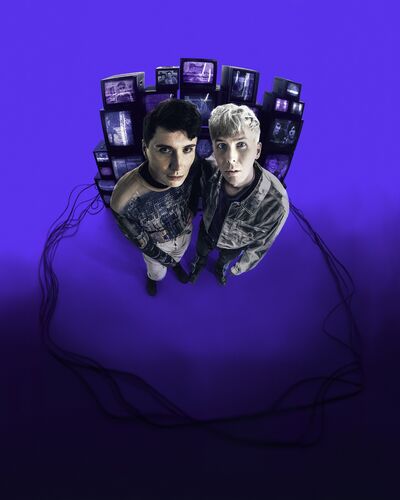 Dan and Phil standing in front of a stack of screens encircled in wires