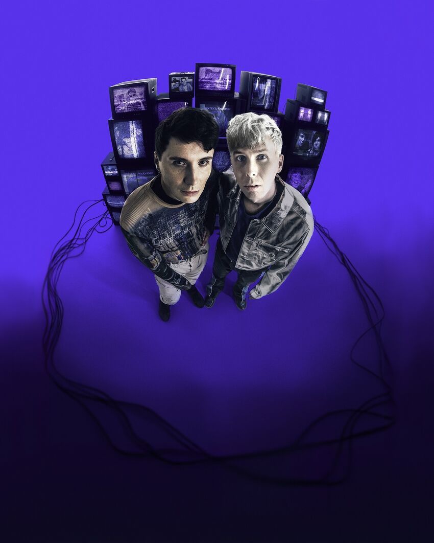 Dan and Phil standing in front of a stack of screens encircled in wires