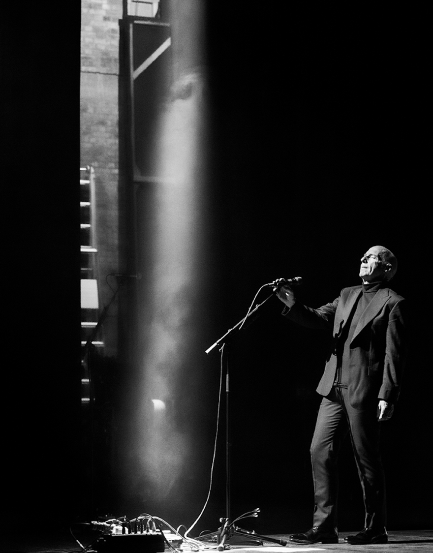 Black and white photograph of Midge Ure holding a microphone on stage