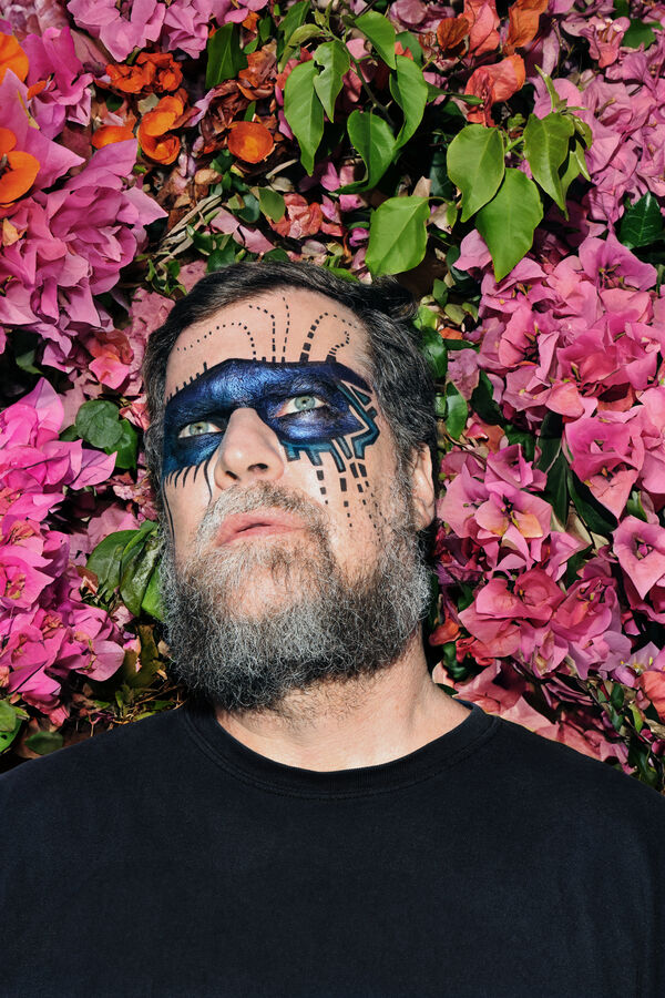 John Grant with face paint against a bed of flowers