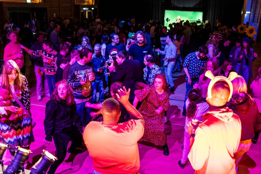 Group of people dancing in a room with purple lights